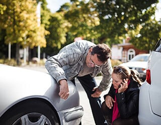 Women talks on the phone while kneeling by her car after a rear end collision.