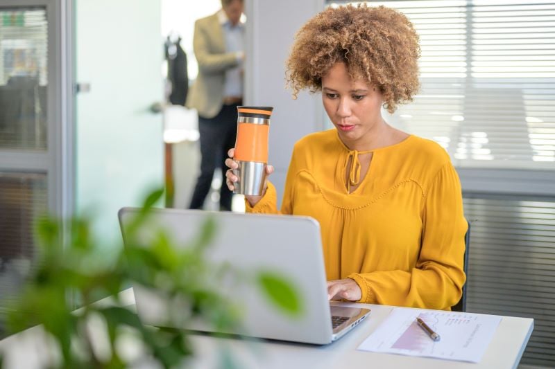 woman drinking coffee at her desk working on a computer.